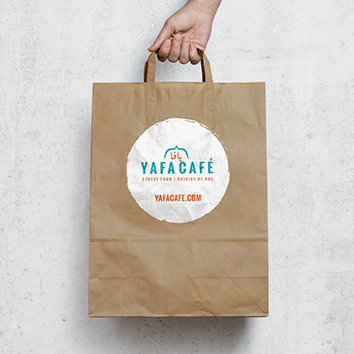 Hand holding a brown paper bag from Yafa Cafe.